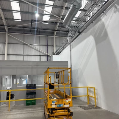 Yellow cherry picker inside food manufacturing facility with HVAC pipework in ceiling